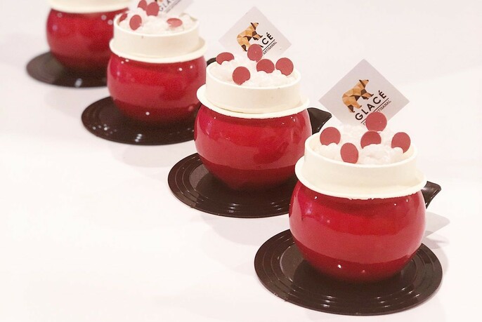 Four red pots with white dessert, topped with small red disks.