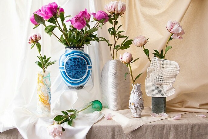 Six vases of differing sizes with flowers against a cream fabric backdrop.