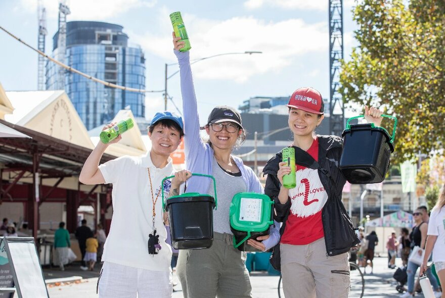 Three Climate Change warriors in the City of Melbourne holding up rolls of compostible bin bags and mini-compost bins. 