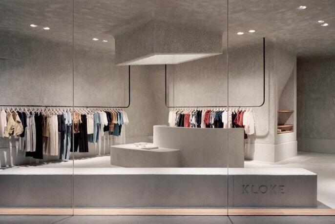 Minimalist retail space with concrete and clothing racks. 