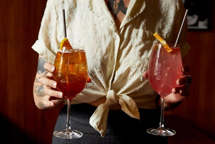A waiter's hands holding two mixed drinks.