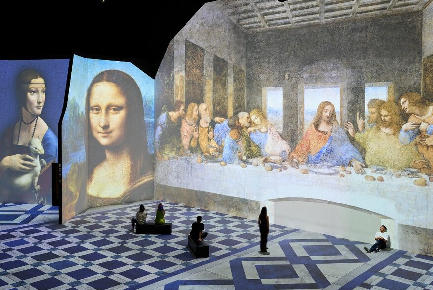 People looking at the Mona Lisa and Last Supper paintings projected on large screens.