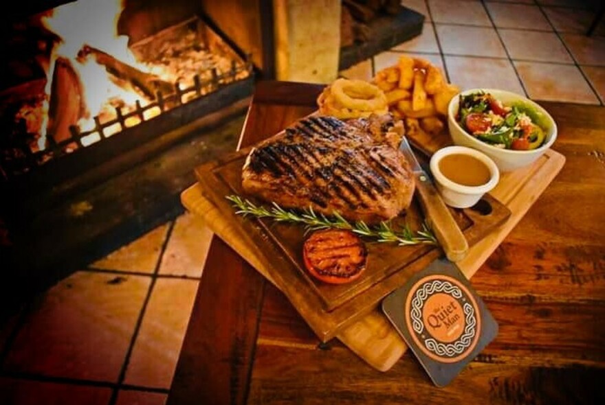 Dining room table in front of an open fire with a platter of meat, chips and salad.