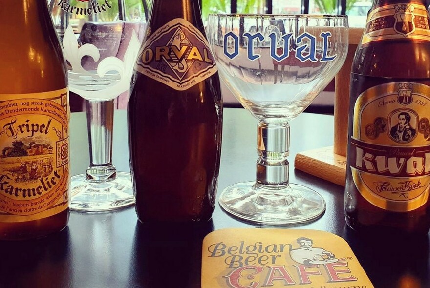 Wooden bar with round beer glasses, beermat and bottles of Belgian beer.