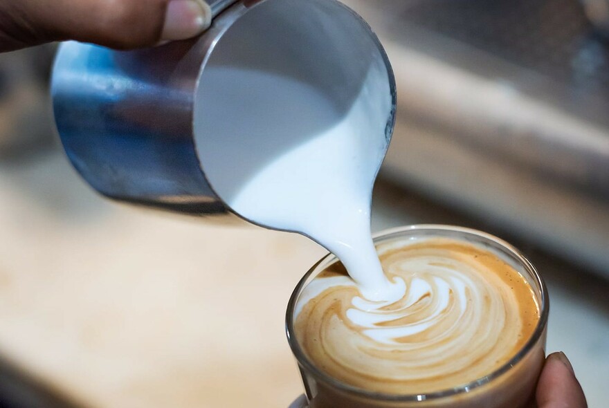 Frothed milk being added to a glass of coffee
