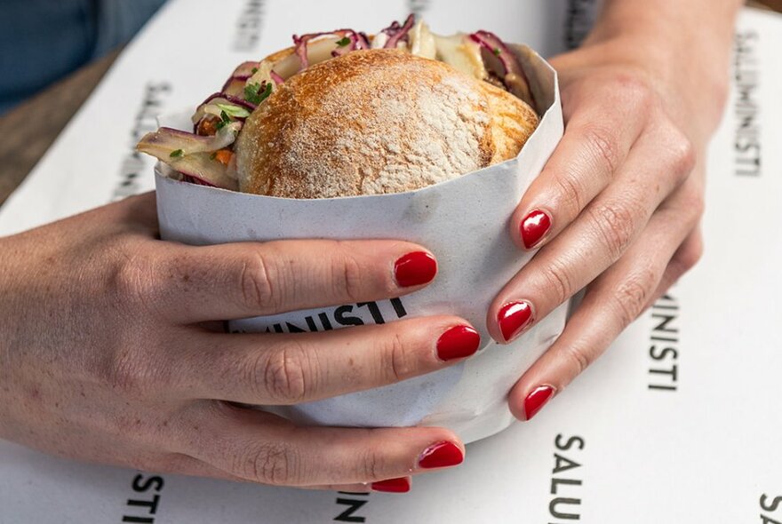 A sourdough breadroll with colourful fillings, being held by a woman's hand with red nail polish.