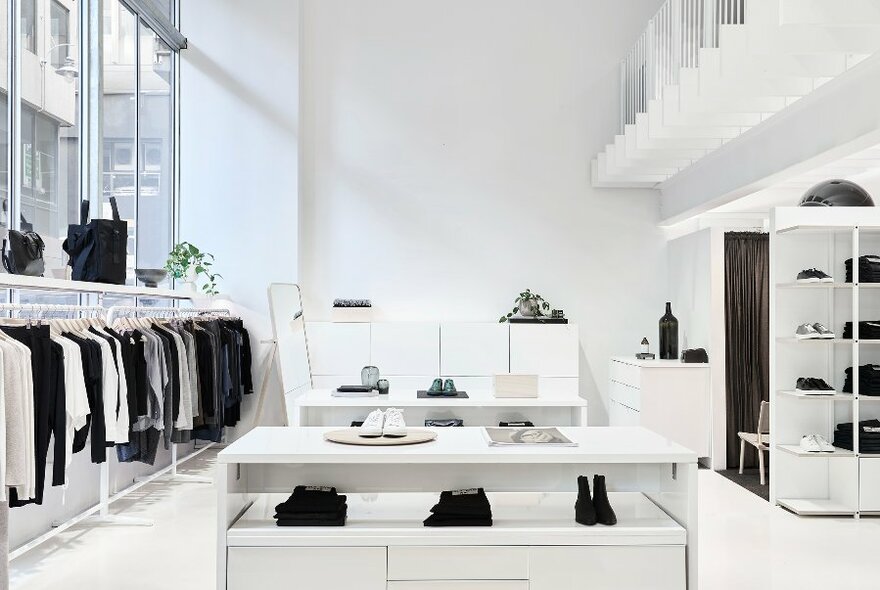 Interior of a fashion store, white walls and fittings, sleek and contemporary with racks of black and white clothes and accessories and a minimalist design.