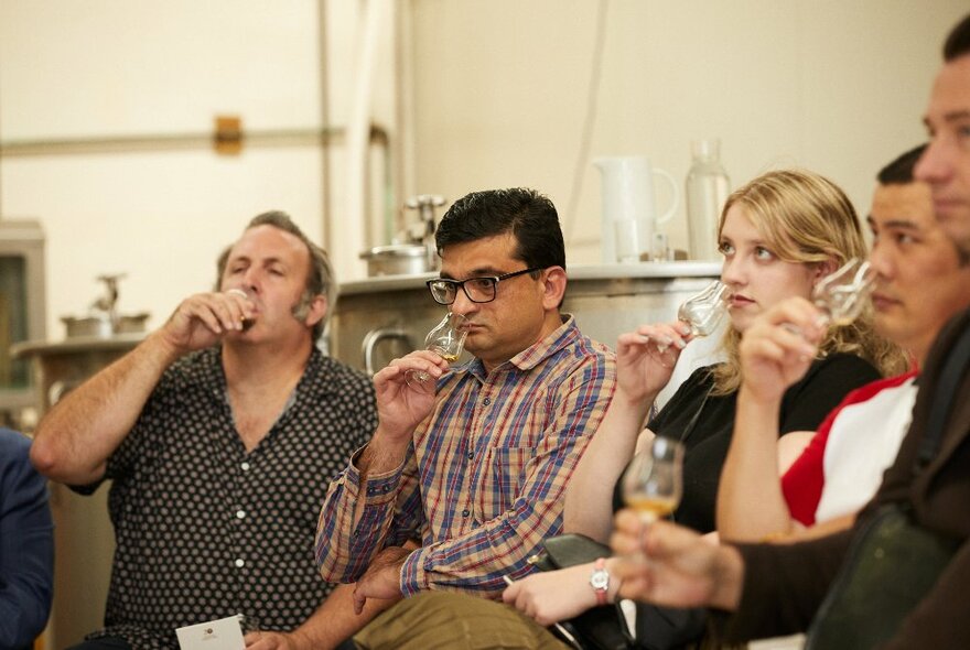 A row of people seated while tasting glasses of whisky.