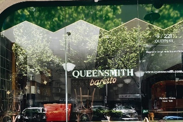 Reflected window of cafe showing the signage that reads QUEENSMITH Baretto.