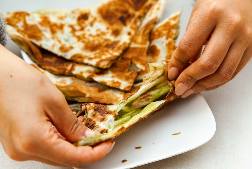 Hands tearing slices of roti bread.