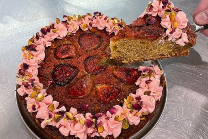 Someone taking a slice of cake decorated with petals and figs.