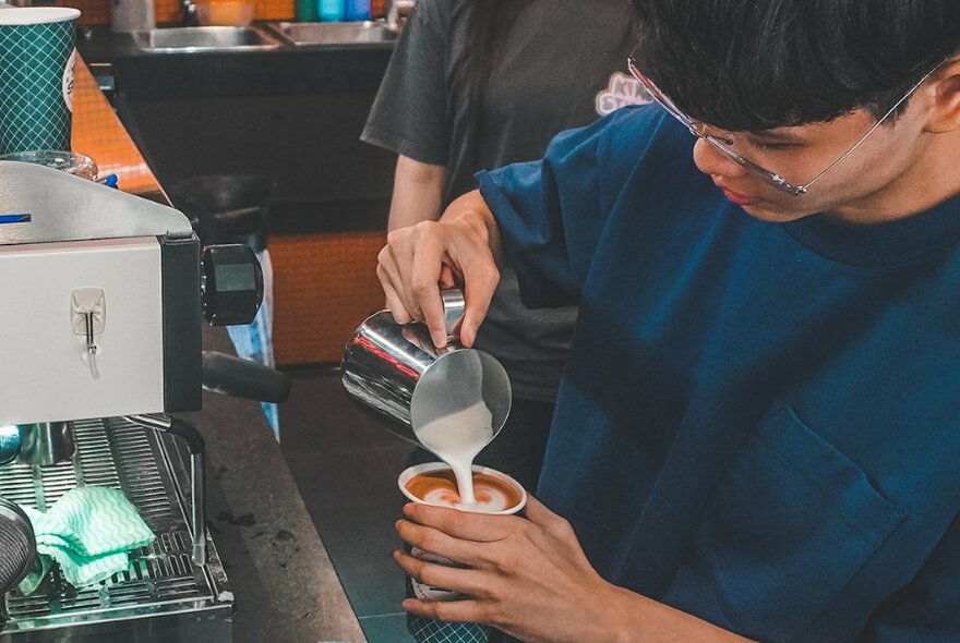 Barista pouring milk into a takeaway cup of coffee.