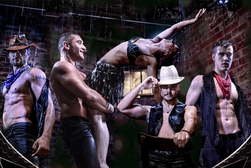 Male and female burlesque dancers in costume, posed in front of a fence and brick wall. 