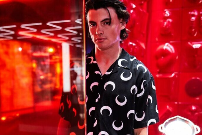 A model in a red room wearing a black short sleeved shirt with moon print. 