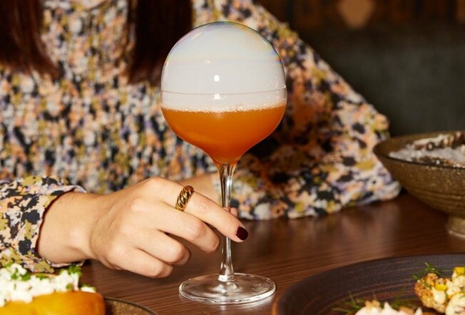 An orange cocktail with a smoke-filled bubble dome on top.