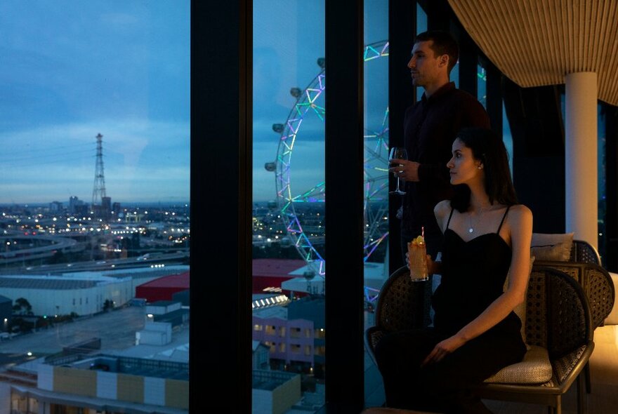 People gazing out of a window that overlooks Melbourne's Docklands at twilight.