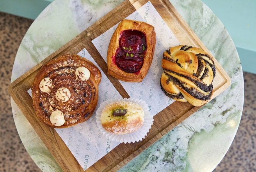 Overhead view of a wooden tray of four sweet pastries, on a small round marble table.
