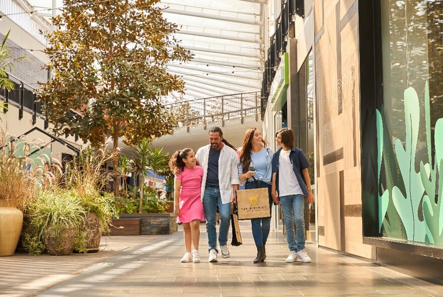 A family walking through an indoor shopping precinct with large potted trees and plants.