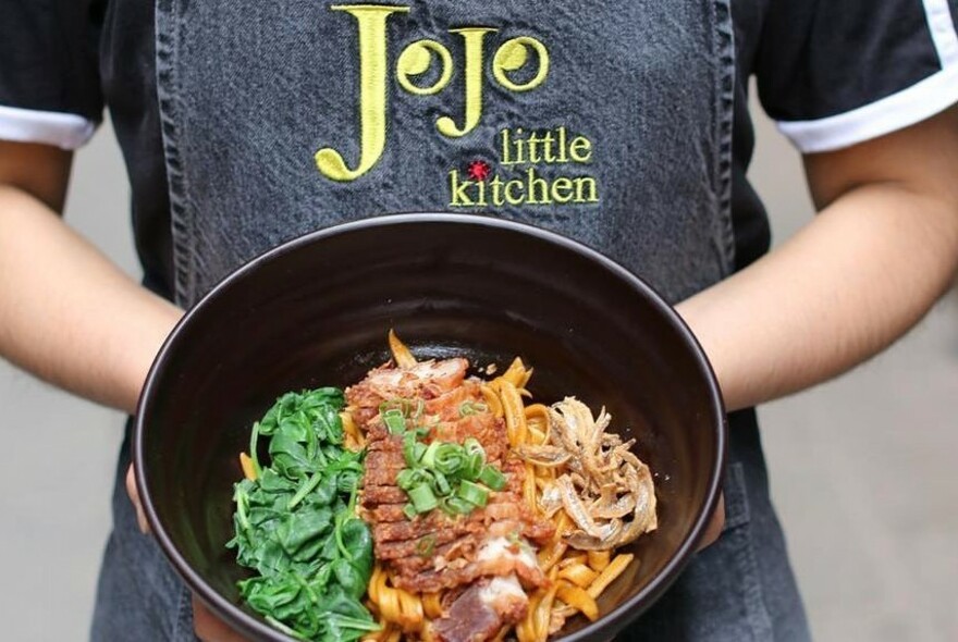 Staff member at Jojo Little Kitchen wearing an apron uniform holding a bowl of food.