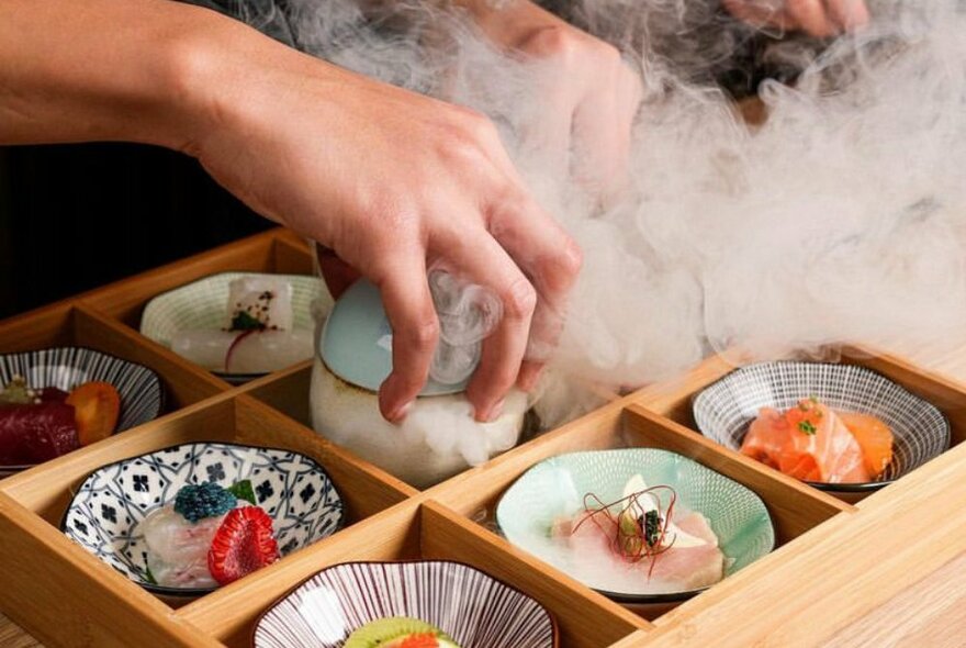 A wooden box with 9 small Japanese dishes with dry ice in the middle,