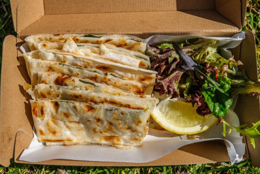 Birds-eye-view of Gozleme in a box with lettuce and lemon.