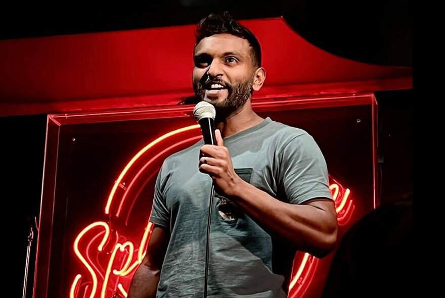 Stand-up comedian Nazeem Hussain holding a microphone and smiling.
