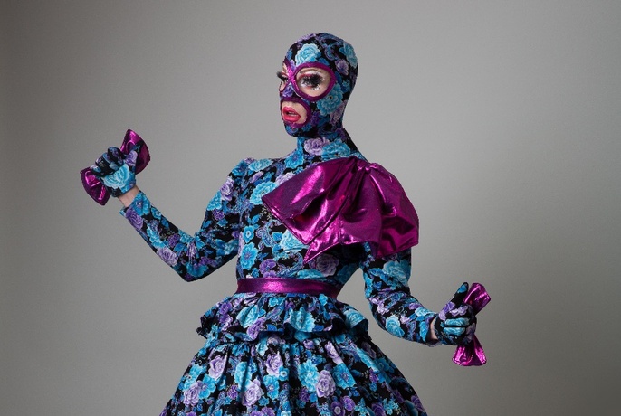 Model wearing Leigh Bowery mask and gown in matching floral blue fabric with purple accents.