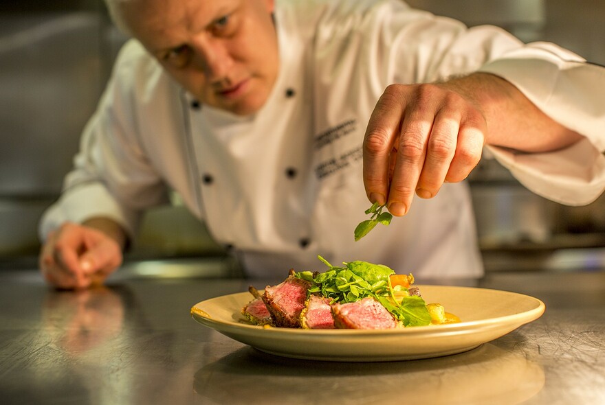 Chef adding a garnish to a plate of meat and salad.