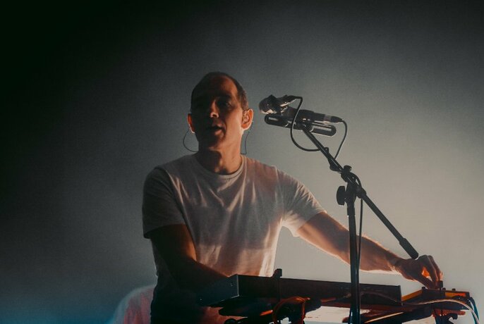 Musician Caribou holding a keyboard in front of a microphone.