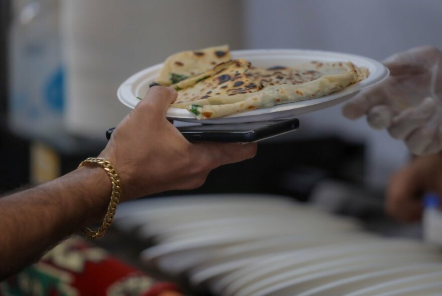 A hand holding a plate of gozleme, filled savoury pastries.