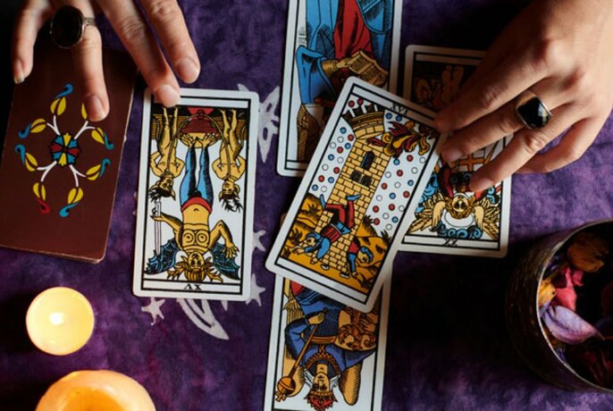 Bird's-eye view of tarot cards on purple cloth, with two hands.