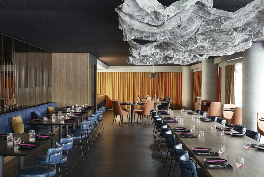 Inside a modern restaurant with blue and tan seats and a large paper sculpture hanging from the ceiling
