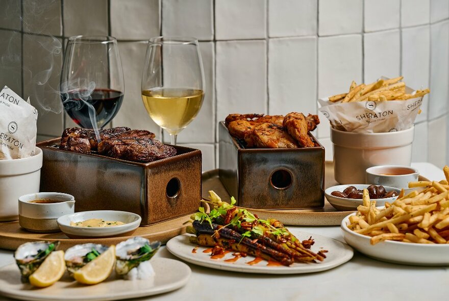 Dishes, ingredients and glasses of wine on a restaurant counter, including oysters and chips.
