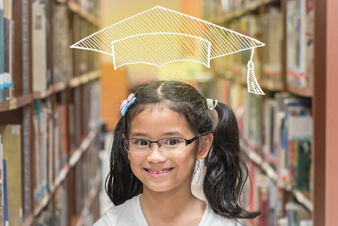 Smiling child, standing between a row of library bookshelves, wearing glasses and with a white line illustration of a graduation mortarboard hat hovering above her head.