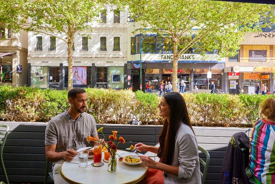 A couple dining on an outdoor table at a city restaurant.