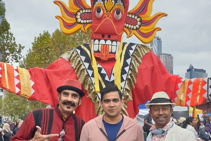 Three people standing in front of a tall dance puppet figure.