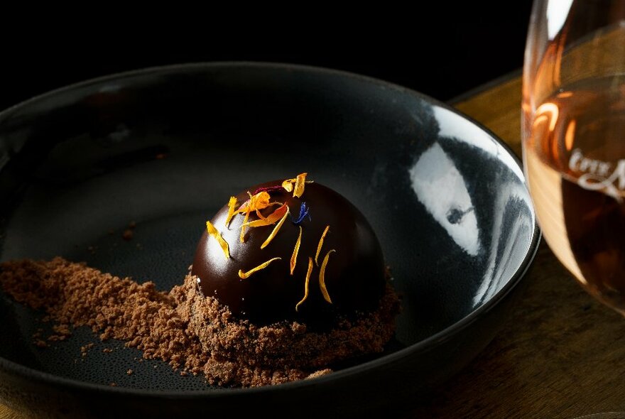 A dark dish with a chocolate dessert and glass of dessert wine.