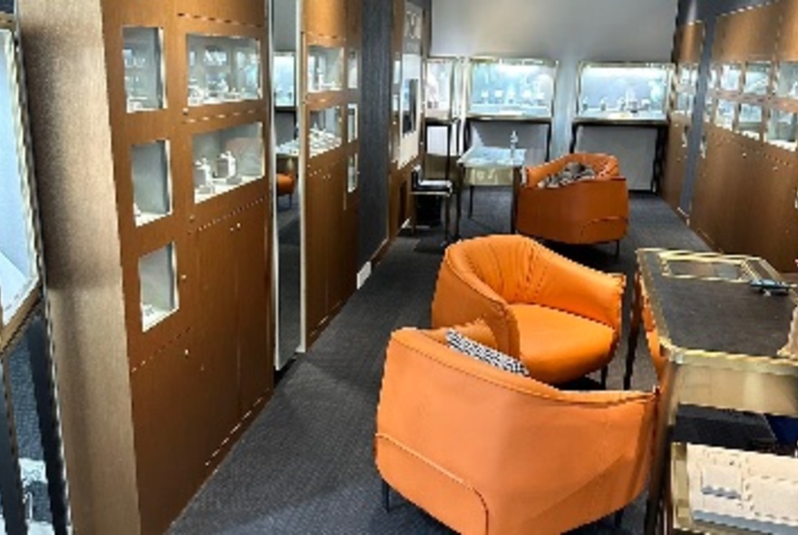 Interior of a jewellery shop with two orange club chairs facing a display table.