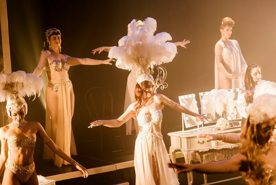 Burlesque dancers performing on stage wearing feather headdresses and white gowns.