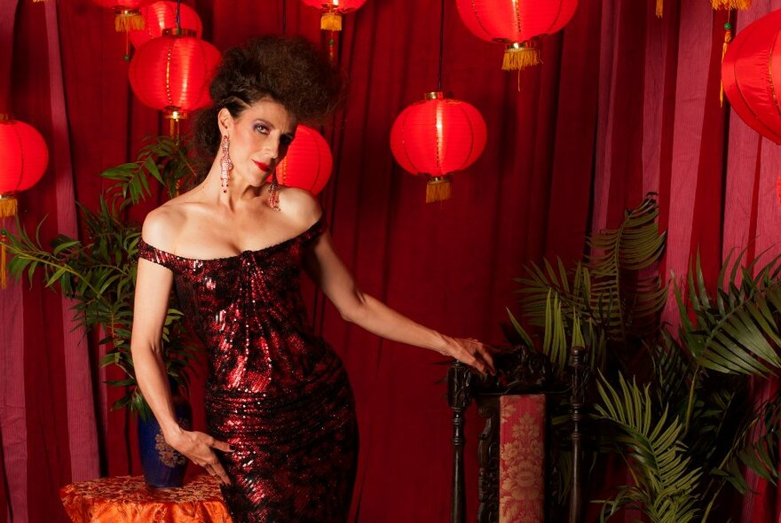 Person wearing a scoop-necked evening gown, standing next to ferns with red lanterns in the background.