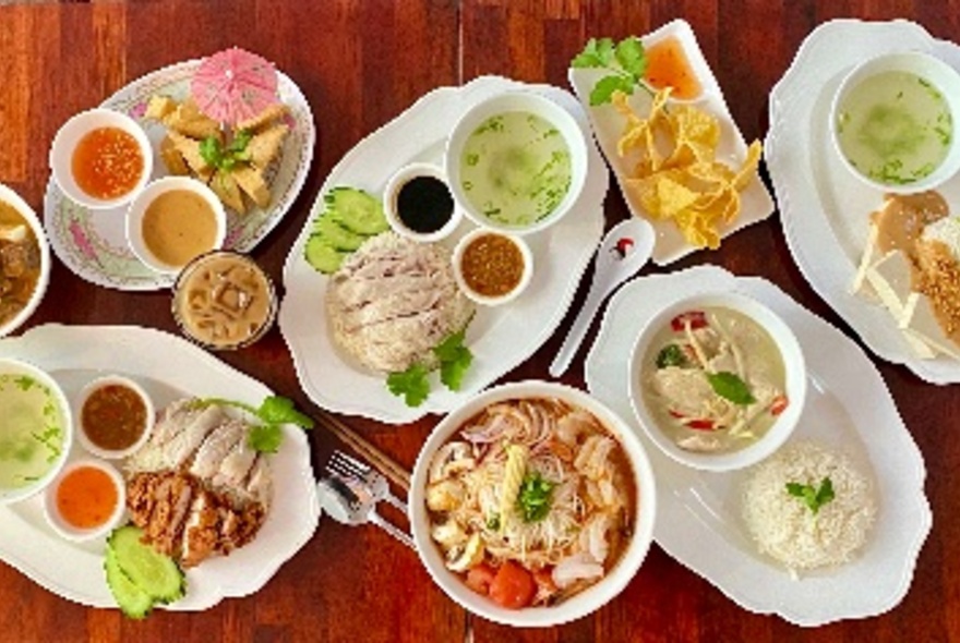 Overhead view of a table featuring large white platters of food including poached chicken, rice, condiments and soups.