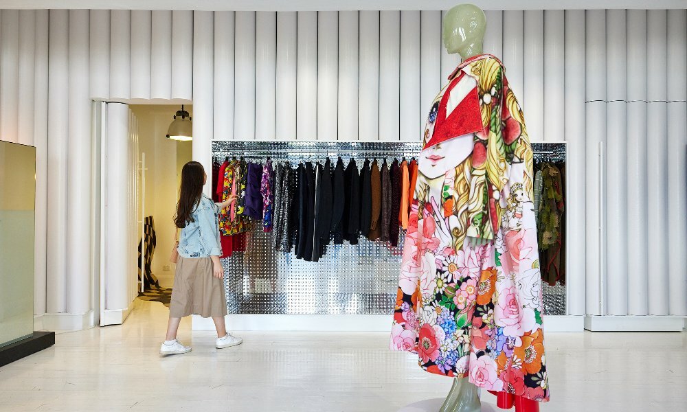 A mannequin is in a shop wearing a kimono and a woman is looking at clothes on a rack