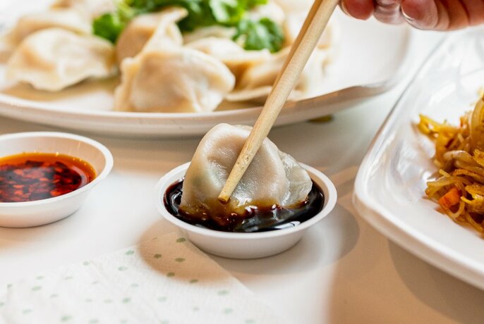 Chopsticks holding a dumpling and dipping it into a small bowl of sauce.