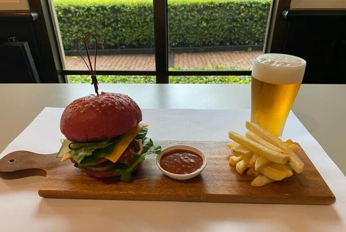 Wooden platter with a hamburger, sauce, chips and glass of beer.