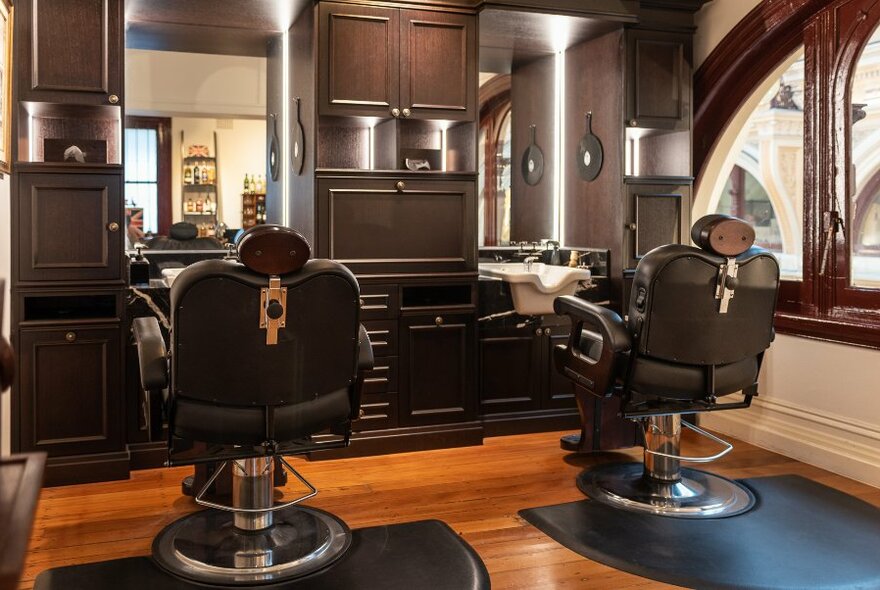 Interior of barbershop with two large reclining barber chairs facing a mirror.