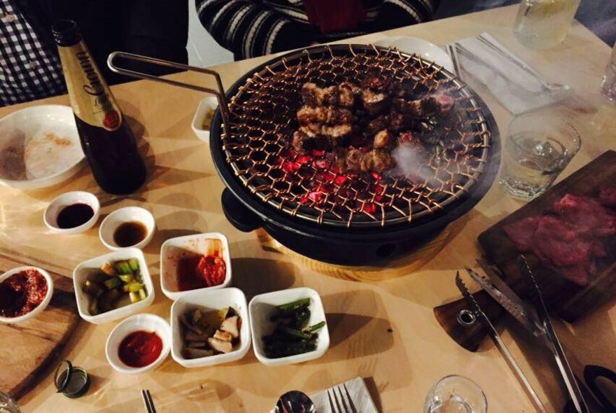 Table set with condiments and meat cooking on a round grill.