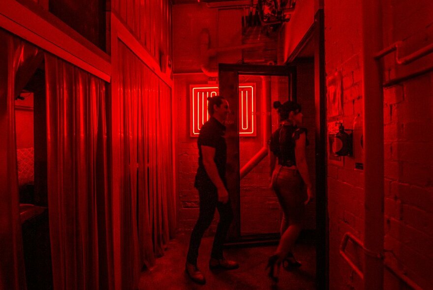 A couple are walking into a restaurant lit in up in dim red lights