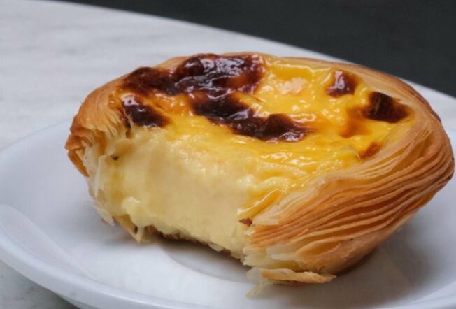 A Portuguese tart on a plate with a bite taken. 