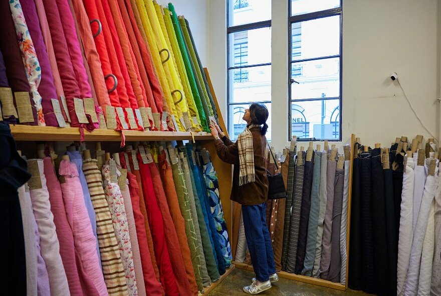 Someone browsing rolls of colourful fabrics in a store.