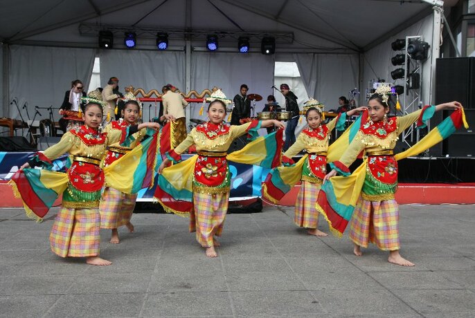 People dancing in Indonesian-style dress in front of a stage.
